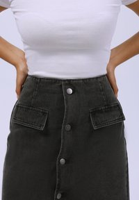 Svart denim skjørt med frontknappe-lukking, to brystlommer og slitesterkt stoff. Skjørtet har et høy midje-design og subtil tekstur.