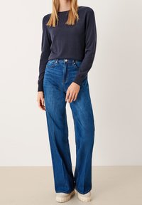 Granatowy sweter z dzianiny zestawiony z wysokim stanem, szerokimi niebieskimi dżinsami. Buty są jasne i mają teksturowaną podeszwę.