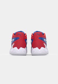 Rode en blauwe sport schoenen met een gestructureerde bovenkant, een opvallend zigzag patroon op de zool en een gewatteerde witte tussenzool. De achterkant toont de ontwerpelementen.