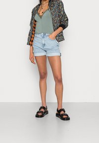 Blommönstrad bomberjacka med svart och orangefoder, grön linnen med spetsdetaljer, ljusblå denimshorts med uppvikta kanter, och svarta sandaler.