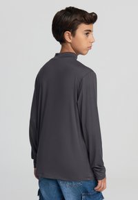 Szara koszula z długim rękawem i wysokim kołnierzem, wykonana z gładkiego materiału. Koszula jest dopasowana przy mankietach i ma luźny krój.