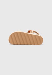 Sandale tressée en tan avec une semelle en caoutchouc plate et striée, ornée d'accents colorés tressés sur les lanières. Texture douce et conception ouverte pour une meilleure respirabilité.