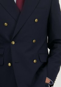 Marineblauwe dubbelgeknoopte blazer met gouden knopen, ingeklapte revers en zijzakken. Gemaakt van een gladde stof met een getailleerde pasvorm.