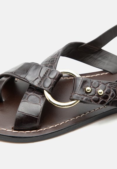 Σκούρο καφέ σανδάλι από δέρμα με λουριά σε υφή κροκοδείλου, λεπτομέρεια με χρυσό κυκλικό κρίκο και διπλά χρυσά καρφιά στην ραμμένη άκρη της σόλας.