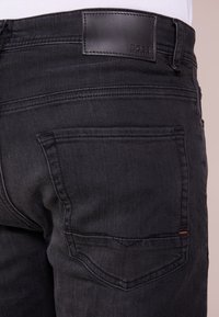 Svarta denimjeans med en läderlapp med "BOSS"-logotyp. Designen inkluderar två bakfickor med subtila sömnadsdetaljer.