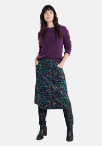 Paars gebreid sweater, rok met bloemenpatroon en zakken, en kniehoge zwarte leren laarzen met blokhakken, tegen een witte achtergrond.