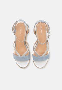 Sandales à talons avec lanières, présentant un dessus en suede bleu clair, des accents métalliques argentés et une semelle intérieure rembourrée beige. La fermeture à boucle est sur le côté.