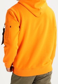Felpa con cappuccio arancione con coulisse, polsini a costine e tasca con zip sulla manica sinistra. Tessuto morbido con una texture liscia.