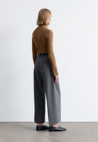 Braun gestreiftes Langarmshirt mit enganliegendem Design, kombiniert mit grauen Weitbein-Hosen und schwarzen flachen Schuhen. Glatte Textur und maßgeschneiderte Passform.