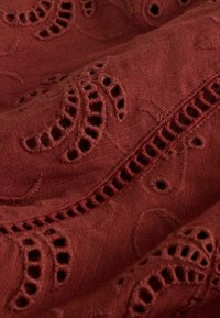 Tissu rouge foncé avec motifs floraux brodés et détails découpés, montrant la texture et les plis superposés.