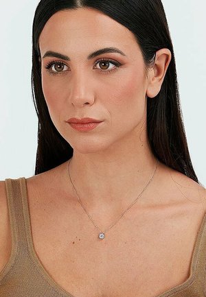 Silberne Halskette mit einem kleinen runden Diamantanhänger, getragen von einer Person vor einem neutralen Hintergrund; sie hat lange dunkle Haare und ein natürliches Make-up.