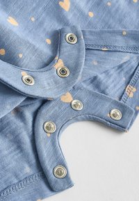 Light blue fabric with orange dot pattern, featuring metallic snap fasteners at the neckline and armholes for easy dressing.