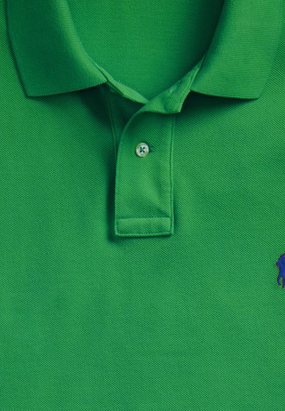 Rohelise polo särgiga, voltidega krae, üks nööp kinnitatud ja väike sinine tikitud logo alumisel paremal küljel.
