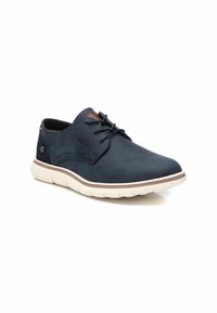 Zapato de cuero azul marino con punta redonda, diseño de cordones y suela blanca suave. Presenta un acento de cuero marrón en la lengüeta y costuras sutiles.