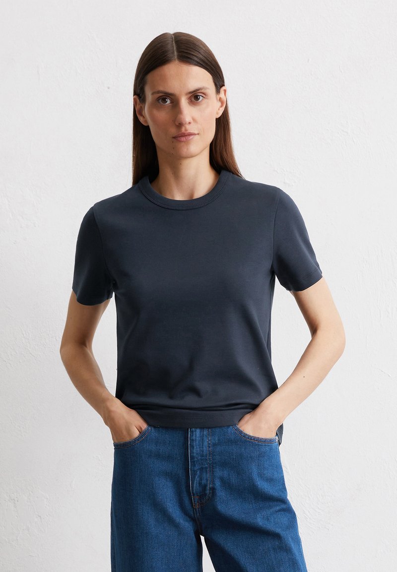 T-shirt navy a maniche corte in tessuto morbido con scollo rotondo; indossato con jeans in denim blu a vita alta con dettagli di cucitura visibili.