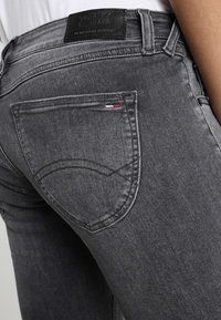 Jeans de mezclilla gris con un diseño de bolsillo trasero curvado y una etiqueta de cuero en la cintura con el nombre de la marca.