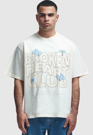 White cotton t-shirt featuring "BROKEN HEART CLUB" printed in bold black and blue letters with heart graphics. Relaxed fit, short sleeves.