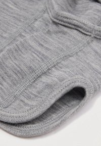 Vestuário ajustado cinza feito de um tecido suave, com uma textura lisa, aberturas redondas e detalhe de costura flatlock ao longo das bordas.