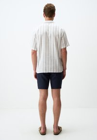 Korte mouwen linnen shirt in lichtbeige met verticale blauwe strepen, gecombineerd met donkerblauwe shorts en bruine sandalen. Minimalistisch ontwerp.