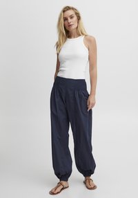 Camiseta sin mangas blanca combinada con pantalones azul marino de corte holgado que presentan una cintura fruncida y puños gather.