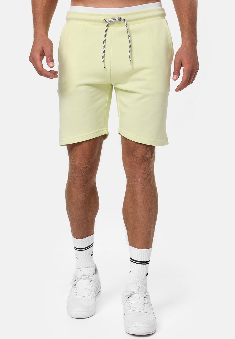 Lys gule bomulds shorts med elastisk talje og sort-hvide snørebånd. Har sidelommer og en afslappet pasform. Hvide sneakers på.
