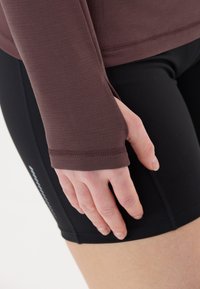 Langærmet, maroon top med tekstureret stof og tommelhuller, parret med tætsiddende sorte shorts, der viser kontrasterende sømme og et strømlinet design.