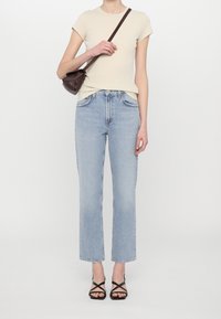 Camiseta Beige de manga corta, jeans rectos de color azul claro, sandalias negras de tiras y un pequeño bolso cruzado marrón.