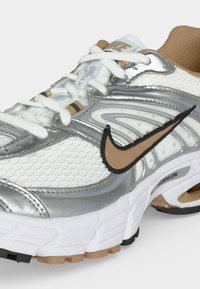 Λευκό και ασημί παπούτσι για τρέξιμο Nike με καφέ λογότυπο σχήματος swoosh, λευκά κορδόνια και λεπτομέρεια μαξιλαρωμένης σόλας σε λευκό φόντο.