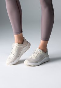 Leichte Sportschuhe in Creme mit strukturiertem Mesh-Obermaterial und gepolsterten Sohlen. Kombiniert mit figurbetonten, hellbraunen Leggings.