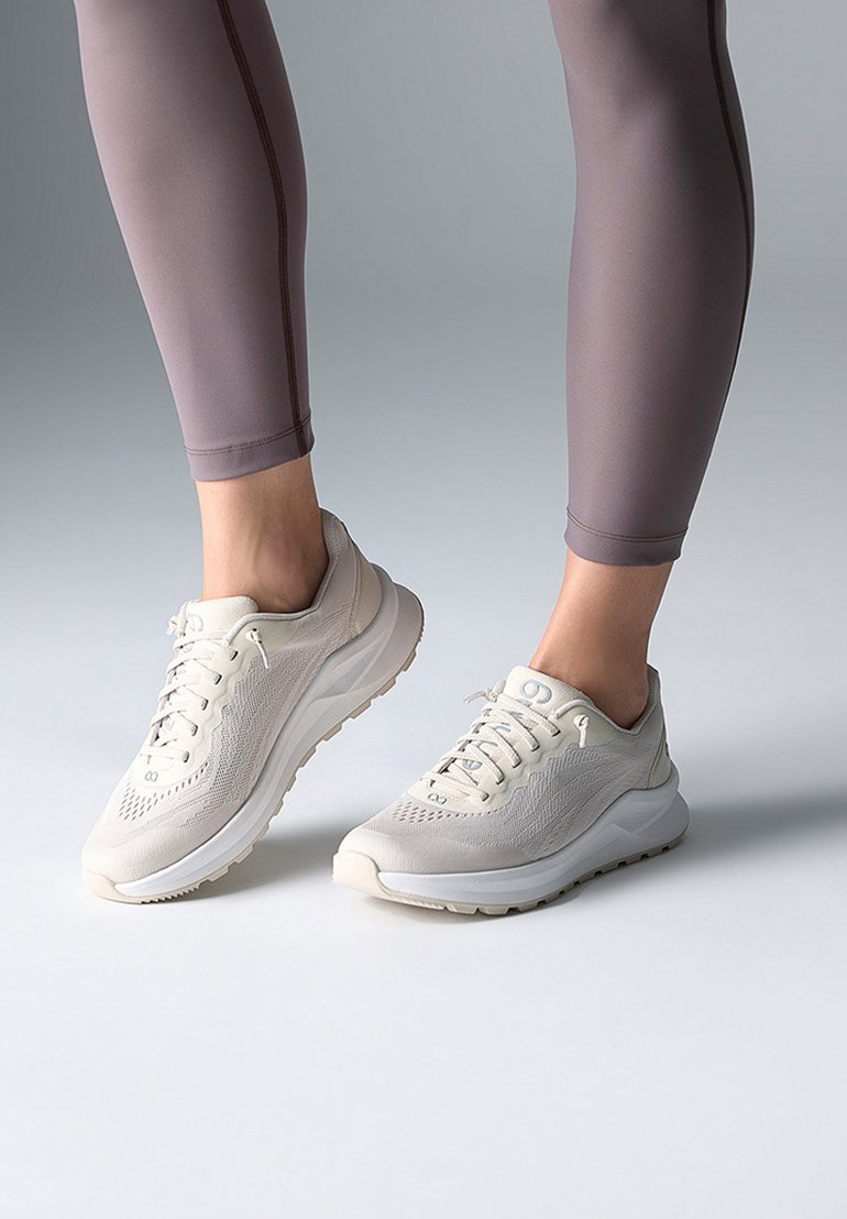 Leichte Sportschuhe in Creme mit strukturiertem Mesh-Obermaterial und gepolsterten Sohlen. Kombiniert mit figurbetonten, hellbraunen Leggings.