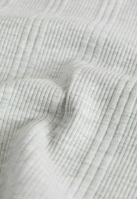 Tissu blanc à côtes avec une texture subtile, présentant de fines rayures verticales. Le matériau semble doux et léger, avec un léger éclat.