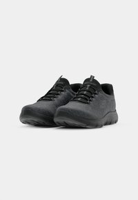 Dark gray athletic shoes made of textured fabric, featuring black laces and a cushioned sole, with a subtle logo on the side.