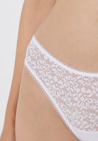 Slips en dentelle blanche avec un motif floral, bords festonnés et taille élastique. Texture douce avec des détails en dentelle délicats.