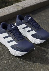 Pair of navy blue and white sports running shoes with laces, placed on asphalt near a stone curb.