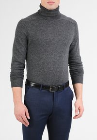 Mørkegrå genser med høy hals laget av strikket stoff, med lange ermer, kombinert med marineblå bukser og et sort lærbelte.
