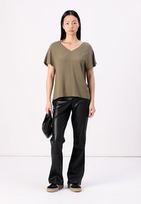 Haut vert olive à manches courtes et décolleté en V associé à un pantalon en simili cuir noir, un sac à main noir et des baskets à plateforme. Texture lisse et coupe décontractée.
