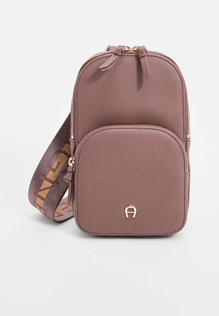 Kleine mauve Crossbody-Tasche aus strukturiertem synthetischem Material, mit einer Vorderreißverschlusstasche und einem dekorativen Riemen mit Logo-Details.