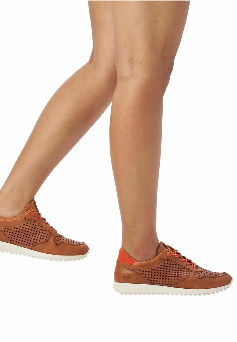 Hnědé kožené tenisky s perforovanými detaily, oranžovými akcenty a bílou gumovou podrážkou. Mají tkaničky a zaoblenou špičku.