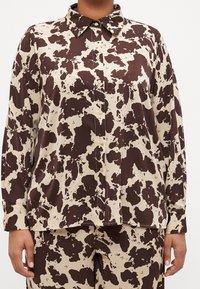 Camicia a bottoni con stampa maculata marrone e crema, maniche lunghe e colletto a punta, realizzata in un tessuto liscio.