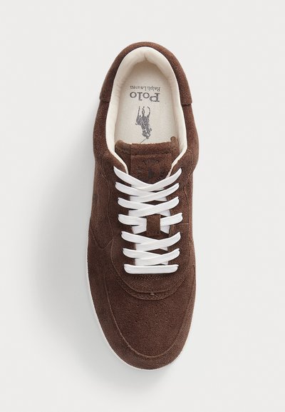 Sneaker in suede marrone con lacci bianchi, punta arrotondata e design minimalista. Presenta un logo sulla soletta e una superficie superiore testurizzata.