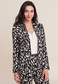 Blazer con stampa animale nera e crema, con taglio su misura, caratterizzato da un rever a punta e maniche lunghe. Abbinato a una semplice maglia bianca.