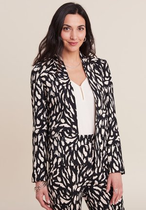 Schwarzer und cremefarbener Animal-Print-Blazer mit tailliertem Schnitt, verziert mit einem Reverskragen und langen Ärmeln. Getragen mit einem schlichten weißen Oberteil.