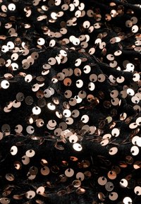 Tissu noir recouvert de sequins circulaires en rose doré brillant, cousus de près, créant une surface texturée et réfléchissante avec une finition éclatante.