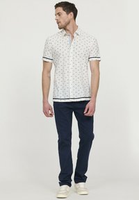 Korte mouwen wit overhemd met blauwe patronen, knoopsluiting, marineblauwe accenten op de mouwen en onderrand. Gepaarde met marineblauwe broek en lichtgekleurde sneakers.