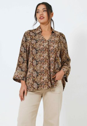Blouse marron à motifs avec un col en V, des manches larges et un tissu texturé comportant des imprimés floraux et de serpent, associée à un pantalon beige clair.