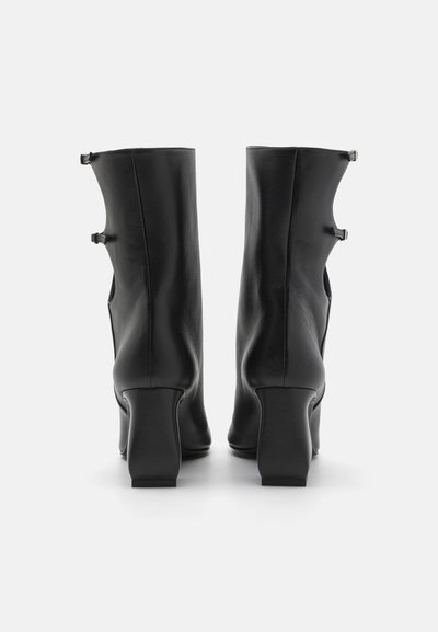 Black leather ankle boots with a smooth texture, featuring a square heel and side buckles for design detail.