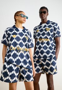 Navy- und weiße gemusterte Polo- und Shorts-Kombination aus glattem Stoff. Mit geometrischem Design, kontrastierendem Kragen und goldenen Logoakzenten.