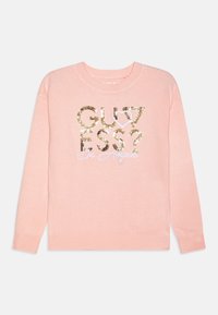Pull rose clair à manches longues, arborant un graphisme en sequins dorés avec les mots "GUESS?" et "Los Angeles" en cursive au centre.