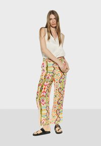 Färgglada mönstrade byxor med lös passform, prydda med geometriska mönster i rosa, grönt och gult. Kombineras med en vit ärmlös topp.