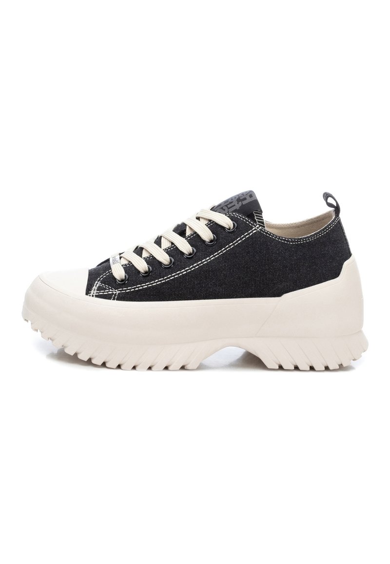 Zapatillas de lona negras con una suela de goma beige gruesa, que cuentan con cordones crema y costuras en contraste. Incluyen una pestaña de agarre en el talón.